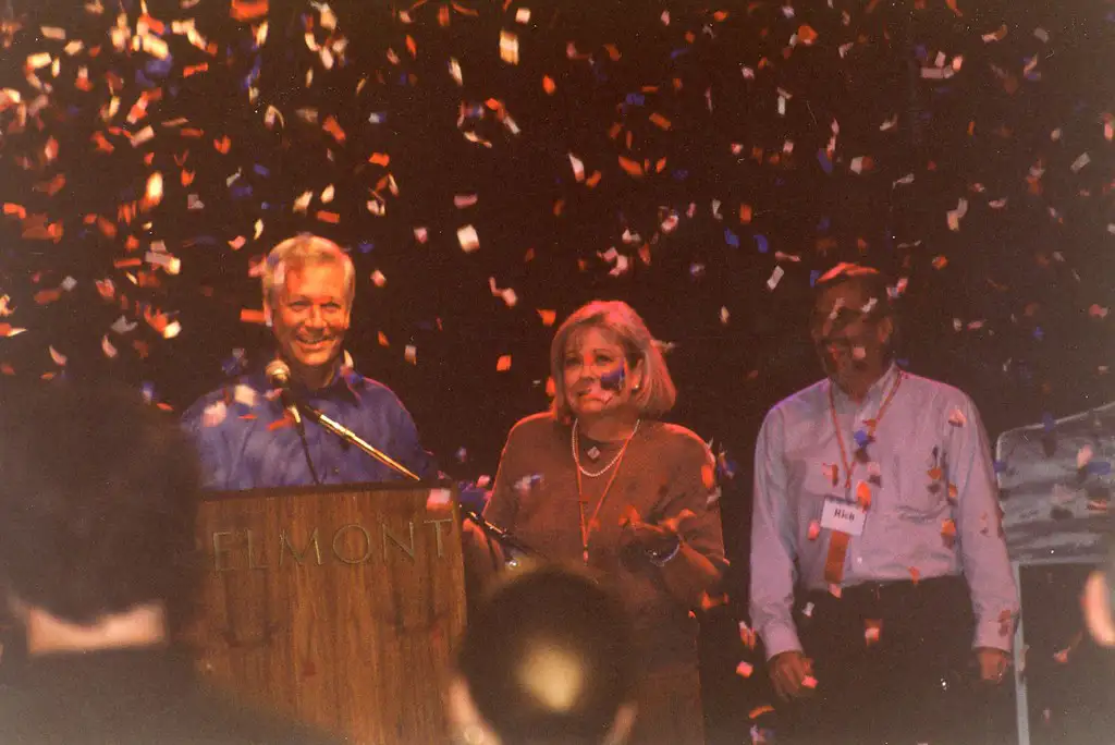 An indoor photo of Bob and Judy Fisher smiling and standing behind a lectern with confetti falling in the air.