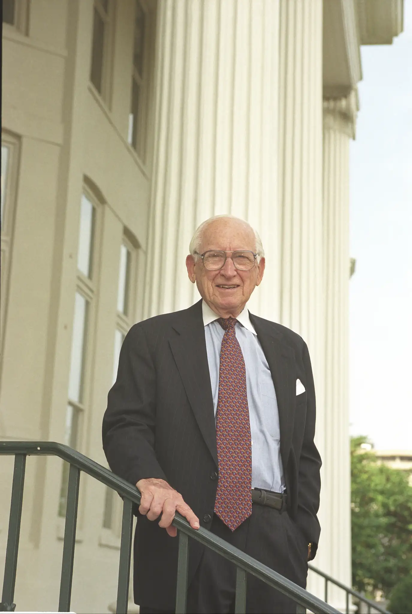 Outdoor photo of Dr. Gabhart standing at the top of the steps and holding the black rail. 