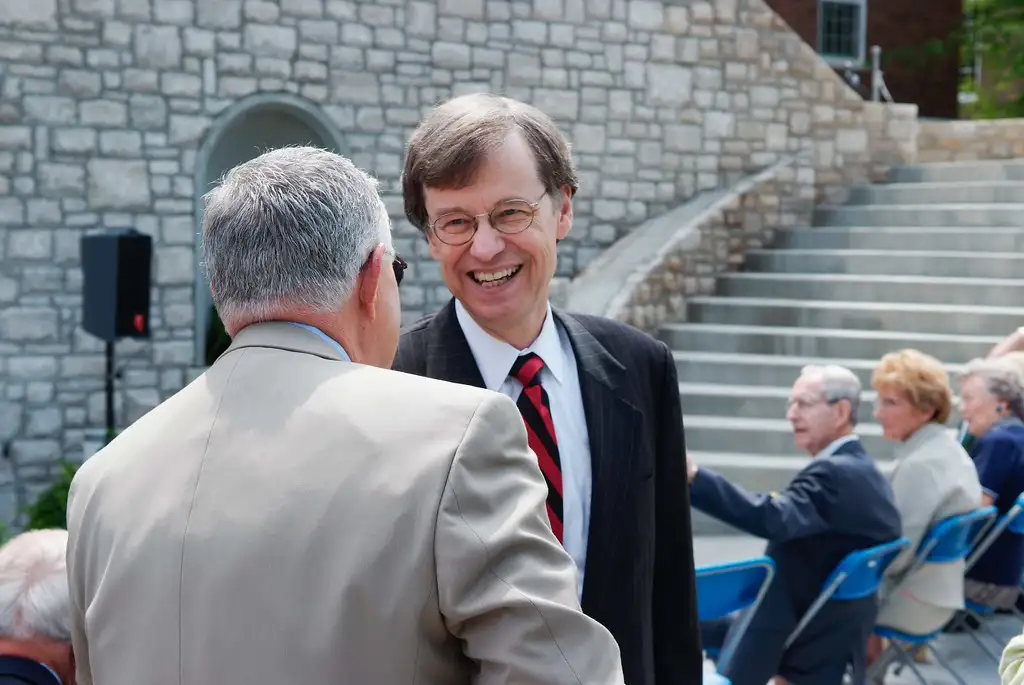 An outdoor photo of Ed Trout smiling in the background and another man facing him and engaging in conversation.