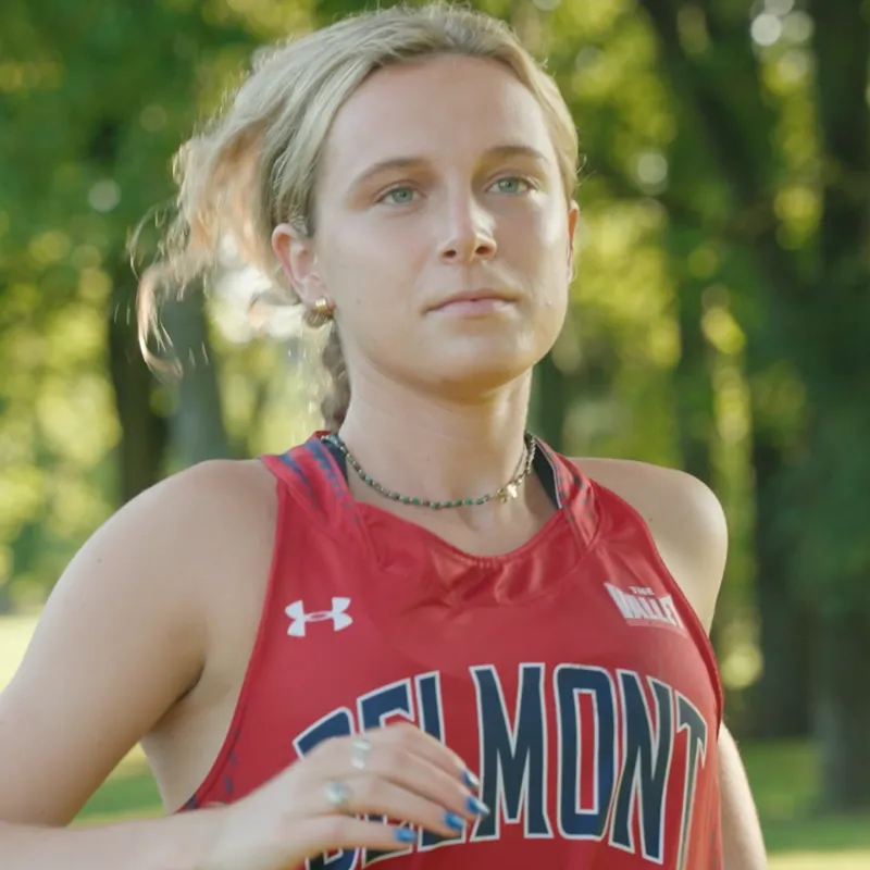 Belmont University cross country runner Grace Litzinger in a red Belmont-branded jersey running outdoors with trees in the background.