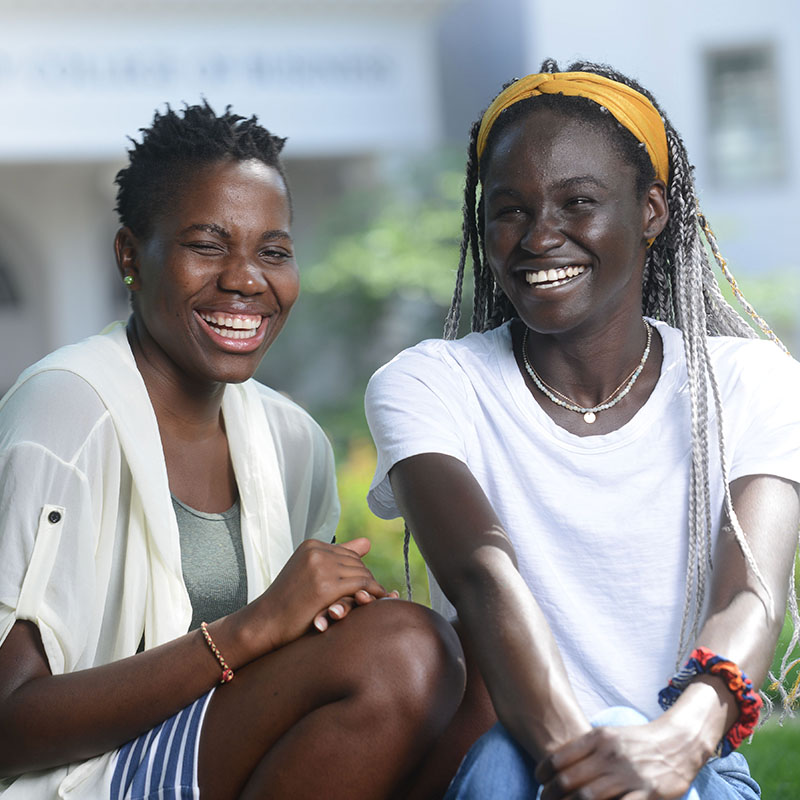 Two students smiling while sitting on grass in the Quad