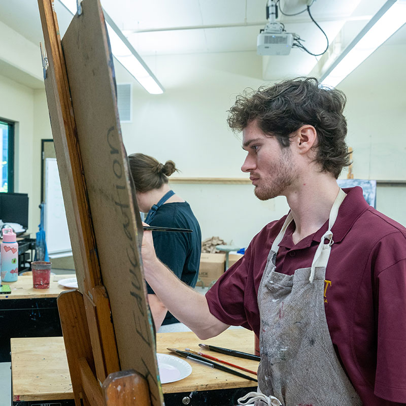A make student painting on a canvas in an Art class