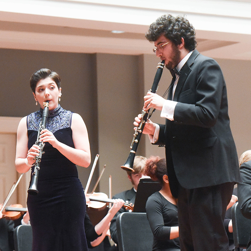 Two students play clarinet on stage in their formal concert wear.