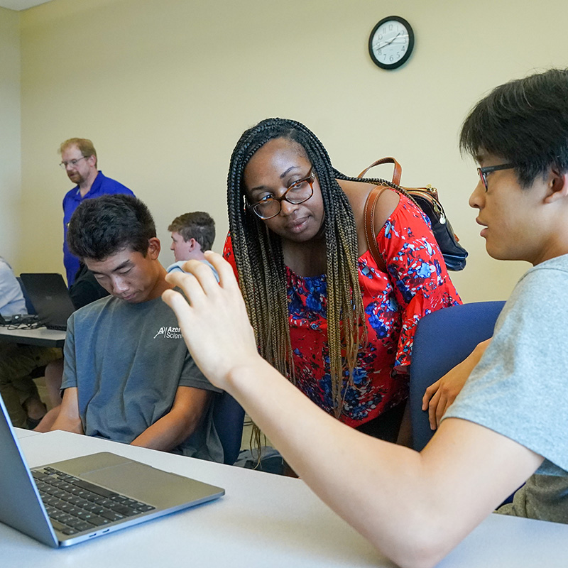 A professor looks over a student's shoulder as he talks with her from his computer.