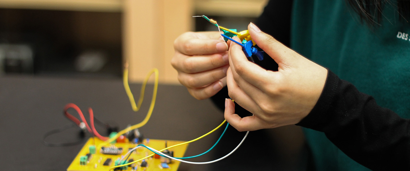 A female student works with wires connected to a circuit board.