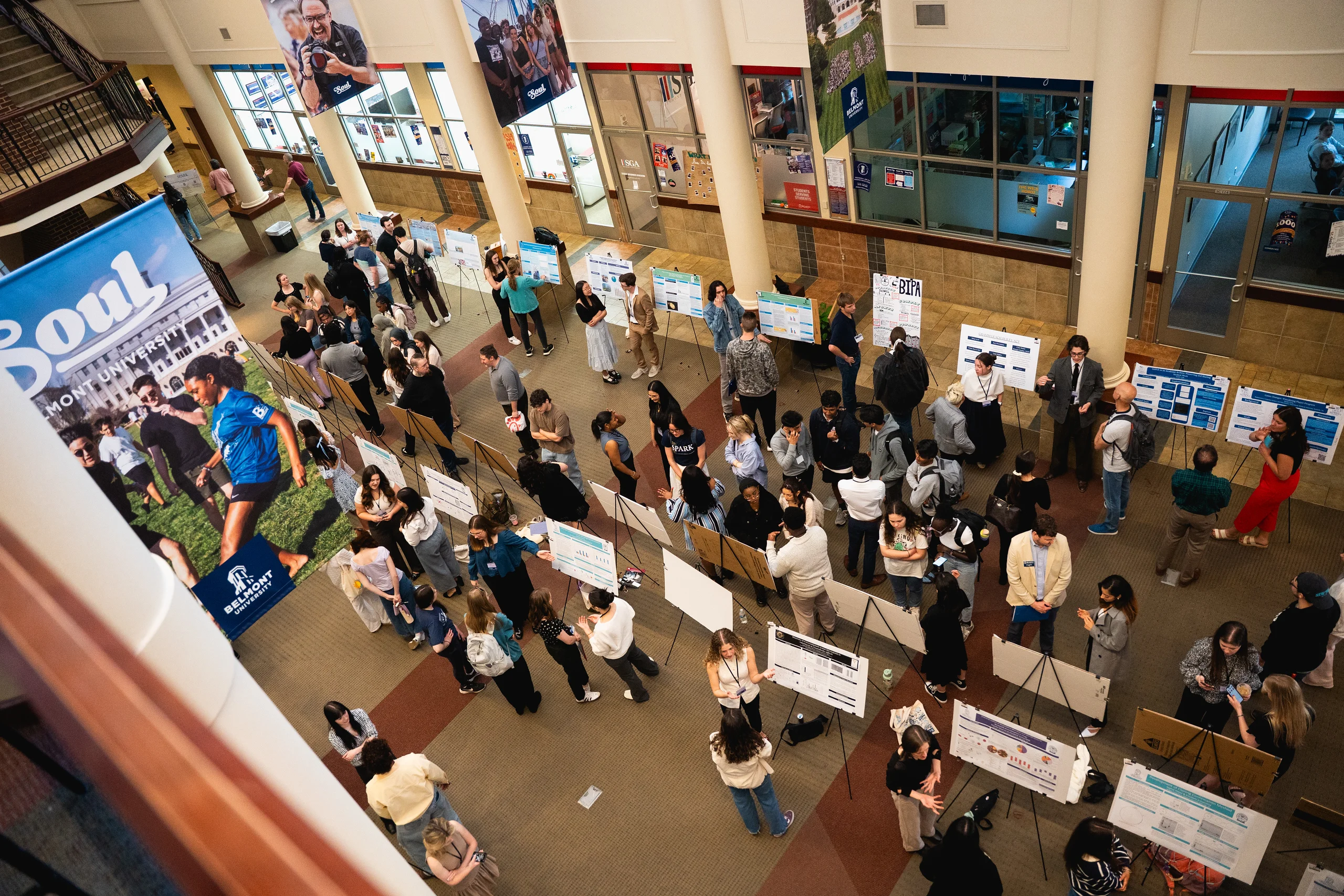 Overhead view of a bustling college fair with students presenting projects on poster boards at Belmont University.