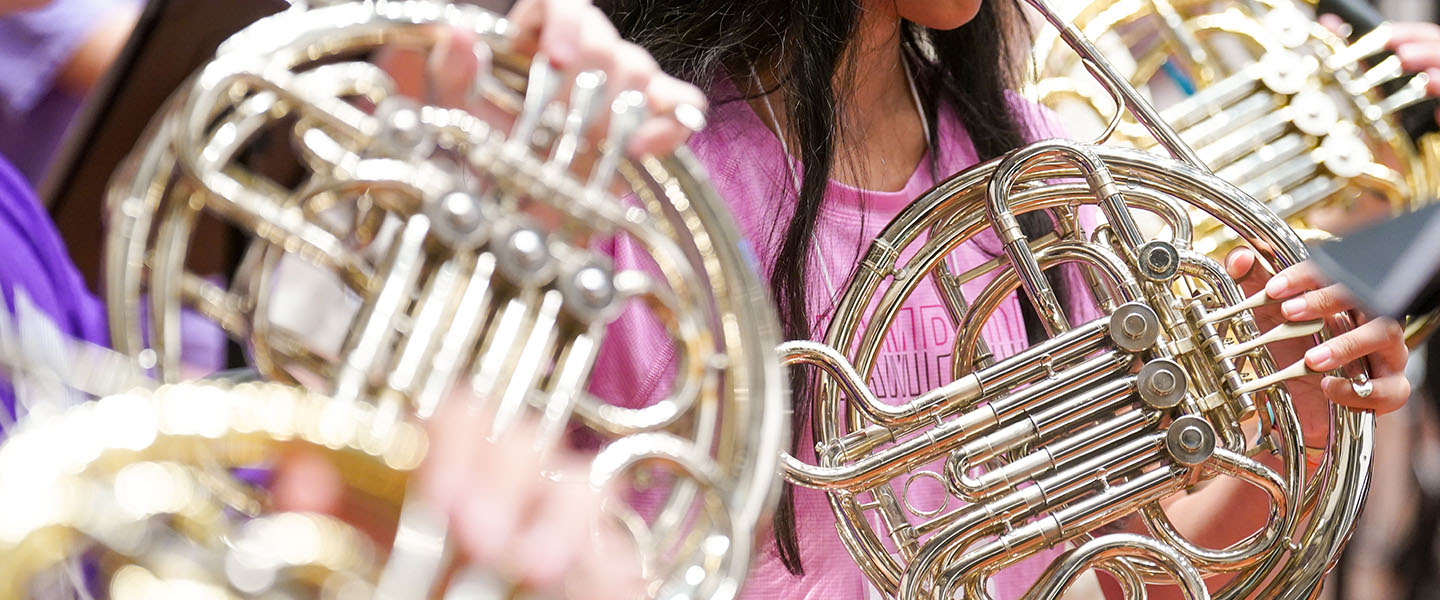 A close-up image of a female student playing the french horn.