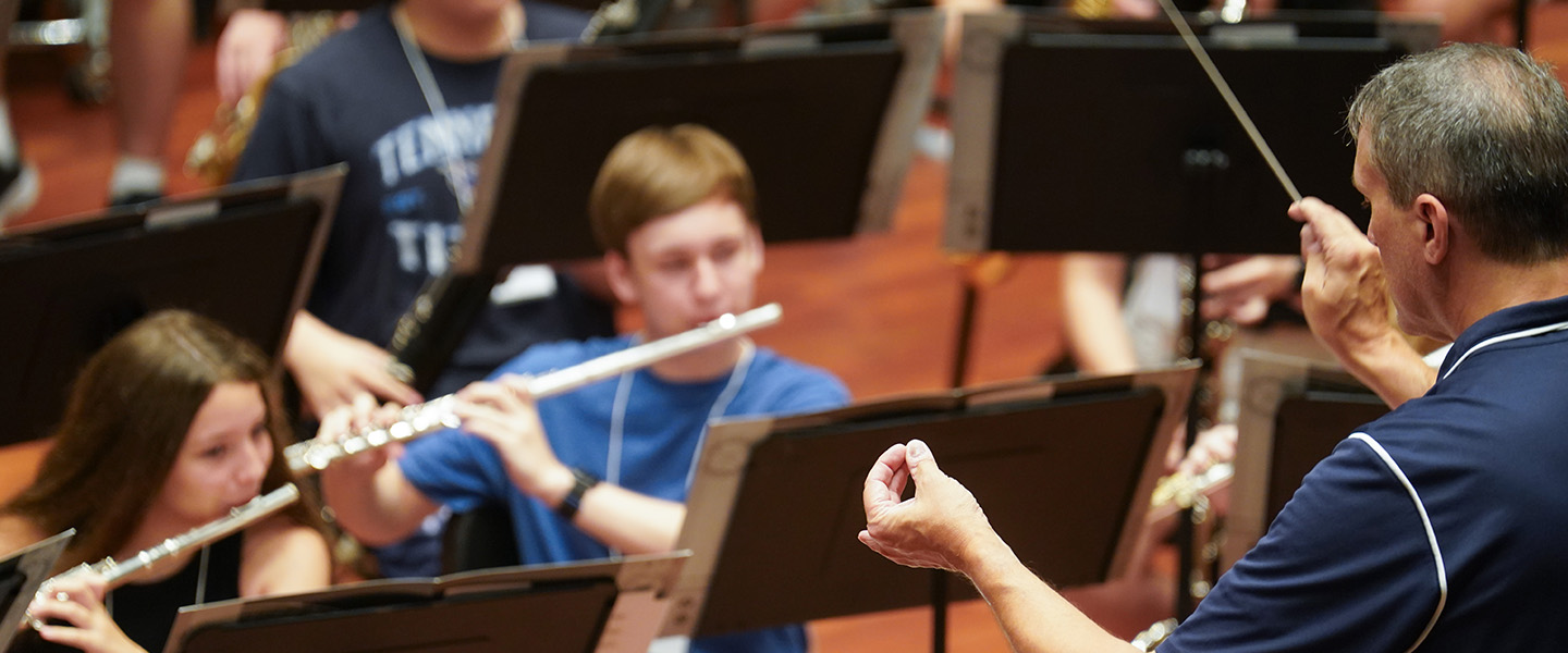 A conductor holds his wand and leads student musicians.