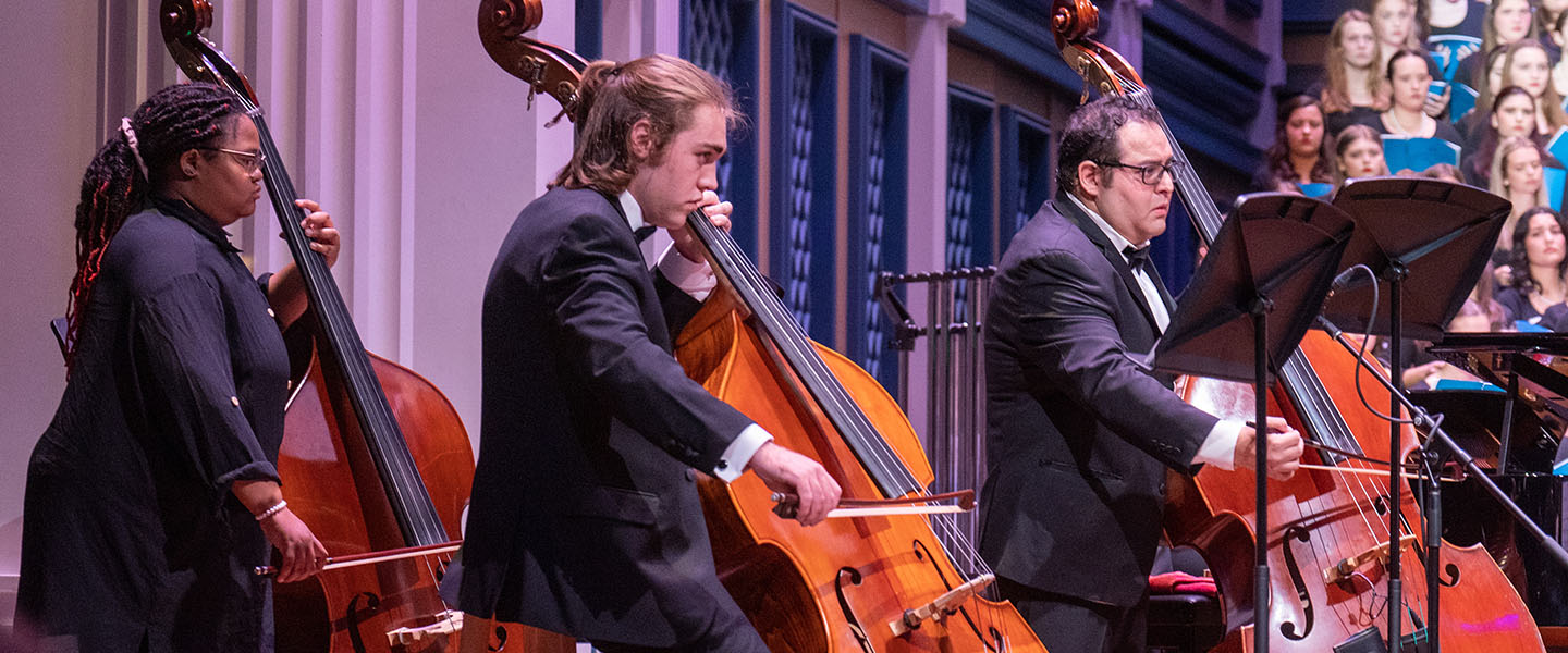 Three music students play upright bass on stage.