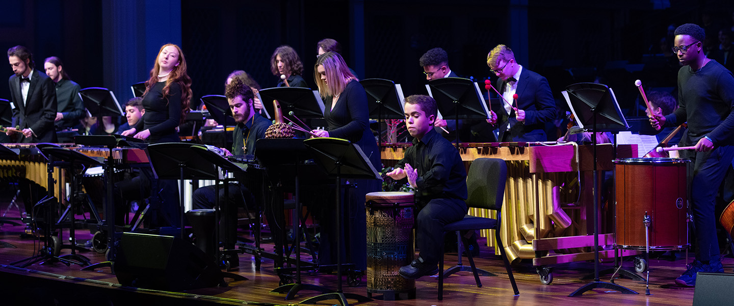 A group of percussion students perform on stage.