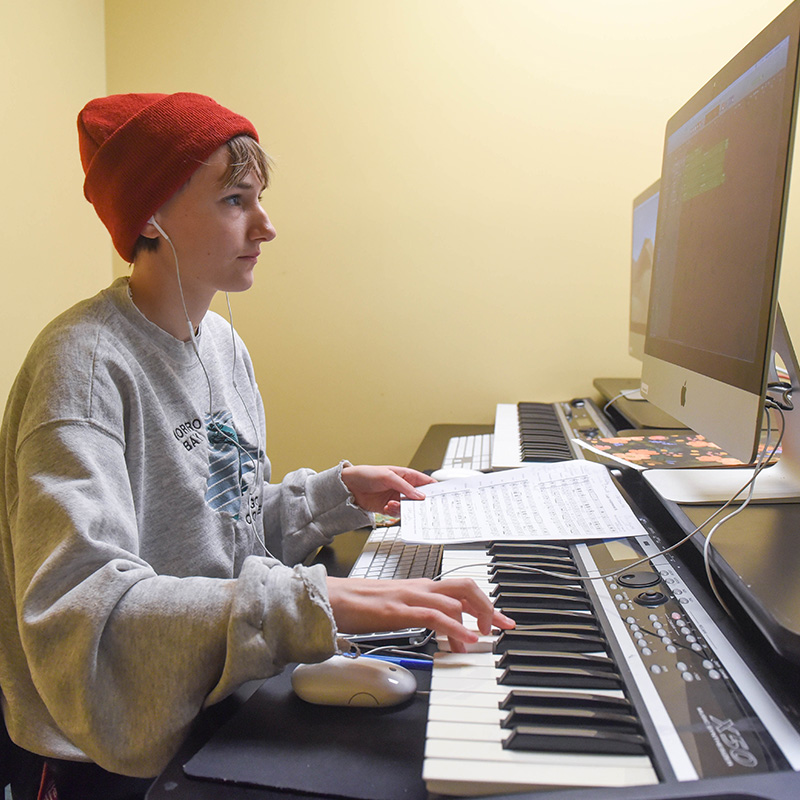 A female student works at a computer with a piano keyboard at her desk.