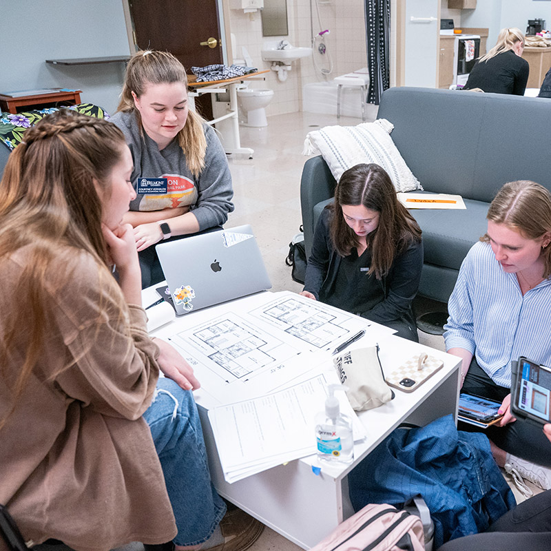 OTD students gathered around a coffee table working on a project in an OTD Home Health lab