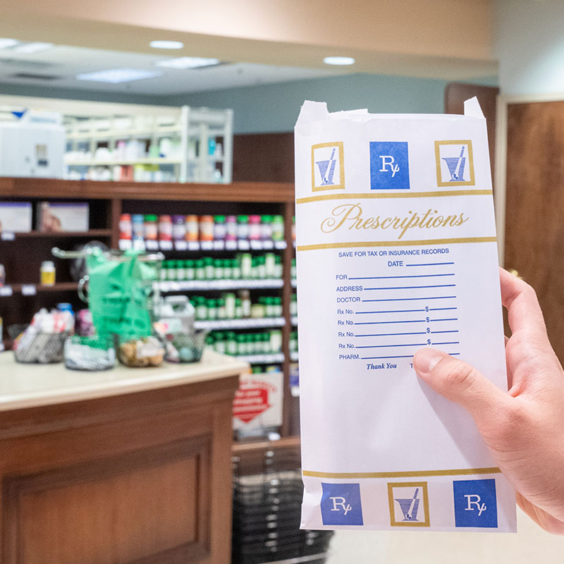 A hand holding a prescription bag in a pharmacy