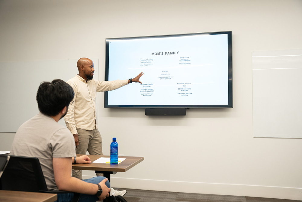 Mental health counseling student presenting in front of the classroom with a screen behind them.