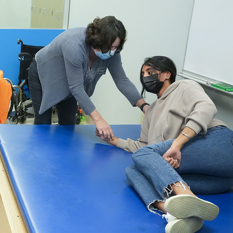 A professor leans over a student lying on a blue medical table.