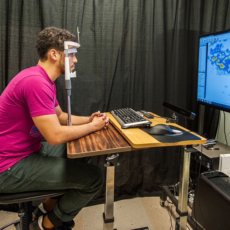 Photo of a male student sitting in front of a screen depicting their brain activity.