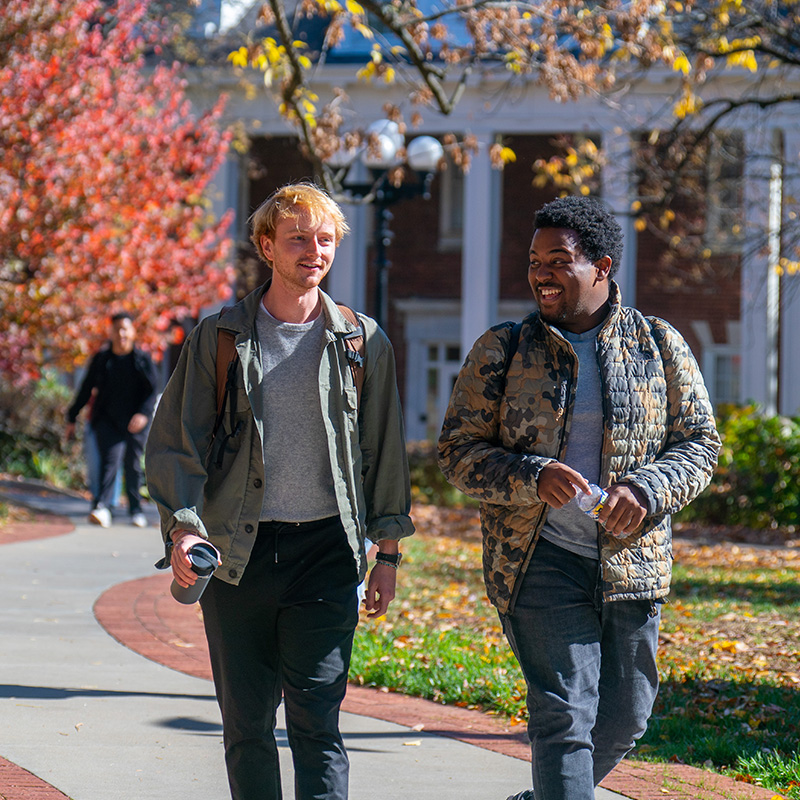 Two male students walking across campus on a fall day