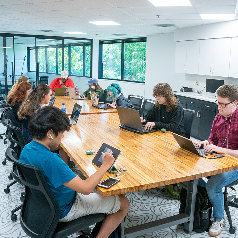 Students working on their computers around a wooden table in an O'More College Studio