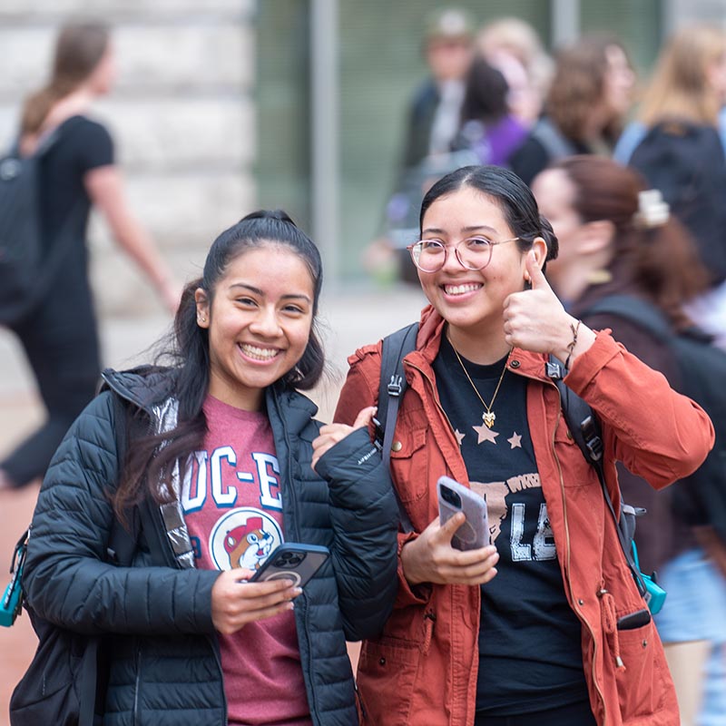 2 students smile for picture while showing a thumbs up.