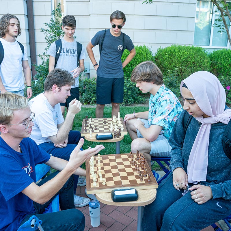 A group of students sitting around a 2 tables with 2 different chess board as the play