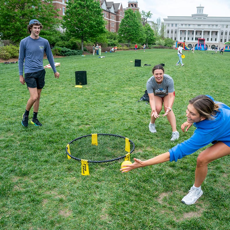 3 students playing spike ball on the lawn