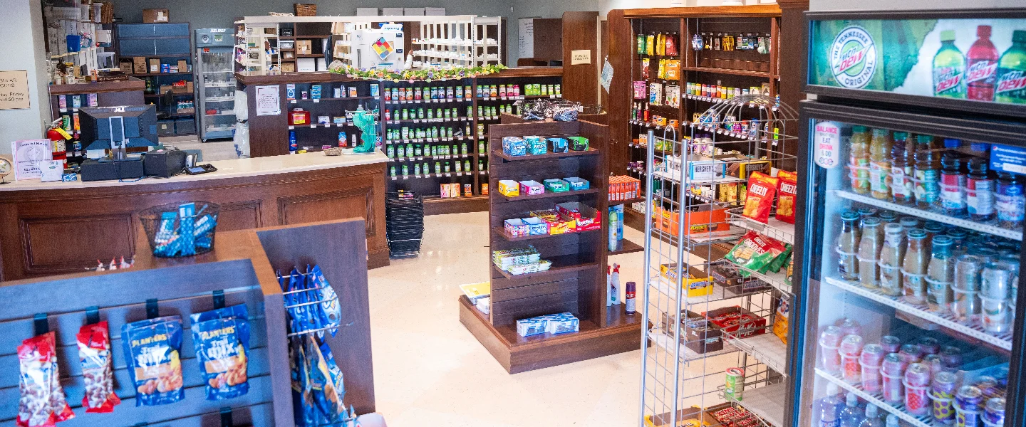 Well-stocked convenience store interior with a checkout counter, refrigerated drinks, and aisles of snacks and various products.