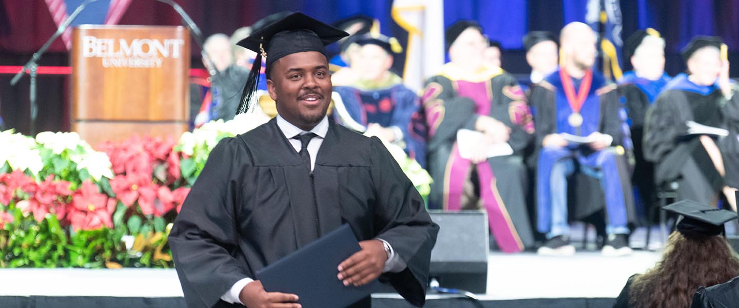 Belmont graduate walking off stage after accepting diploma at graduation while wearing a ca and gown