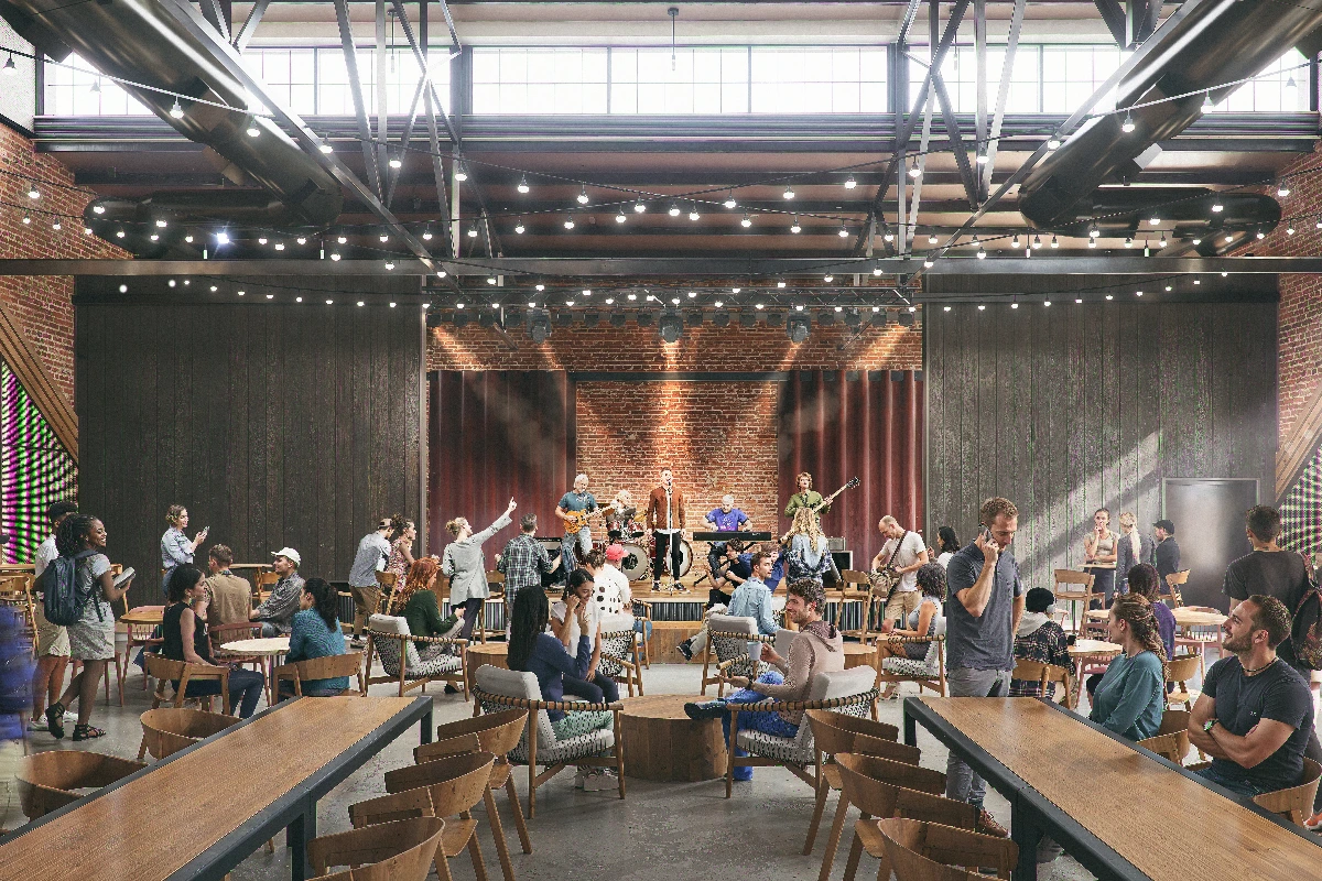 Live band performs on stage in a spacious, industrial-style music venue with a diverse audience enjoying the show.