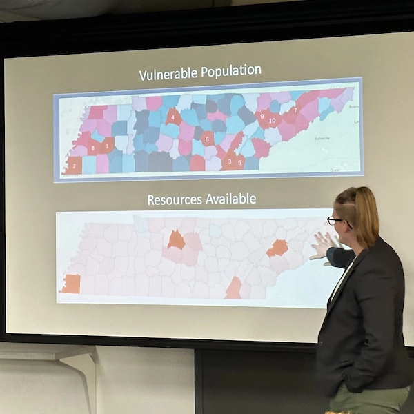 A speaker gesturing to a screen where there is a map referring to vulnerable populations