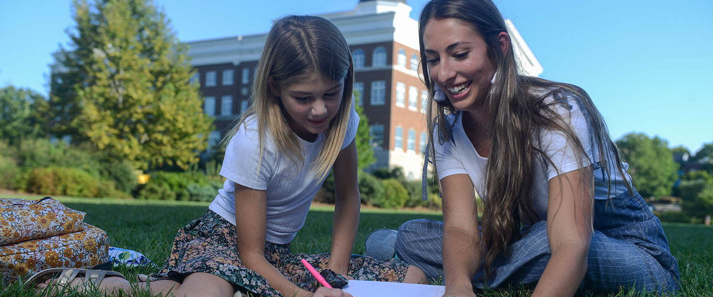 A female student reads with an elementary school student on the Belmont lawn.