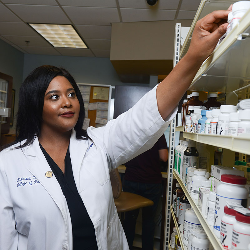 Pharmacy student reaching for pills on a shelf