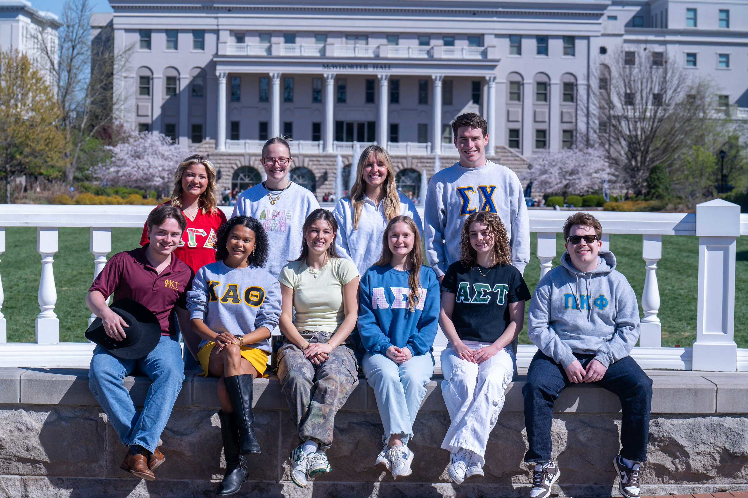 Six students pose and smile at the camera with trees with fall foliage in the background