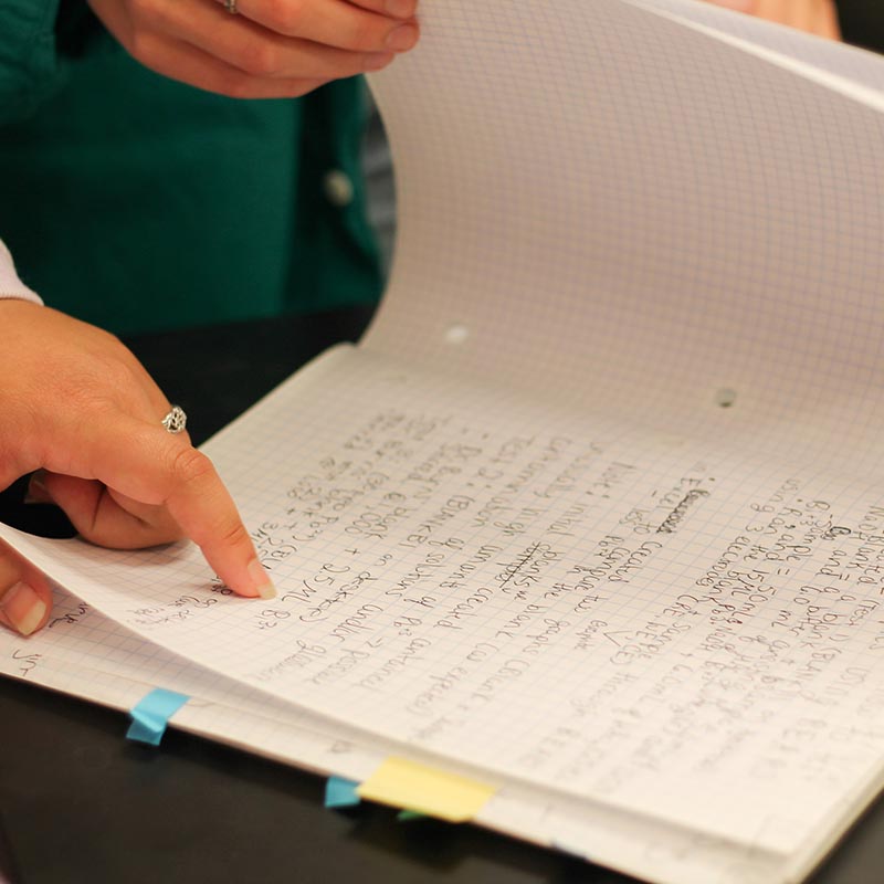 close up of hands flipping through a notebook of handwritten notes. 