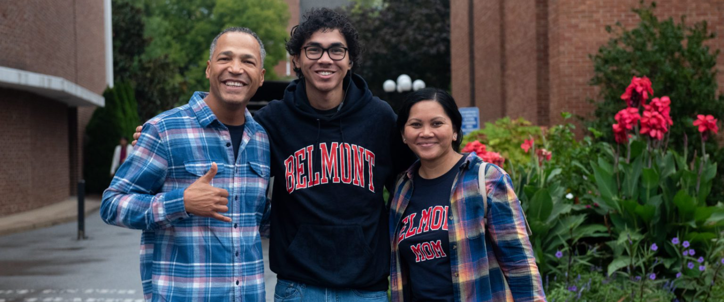 A male student smiles with his mother and father at Parent & Family Weekend outside of the Massey Performing Arts Center.