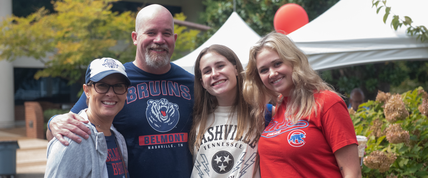 An outdoor picture of a family of two daughters with mother and father wearing various Belmont t-shirts