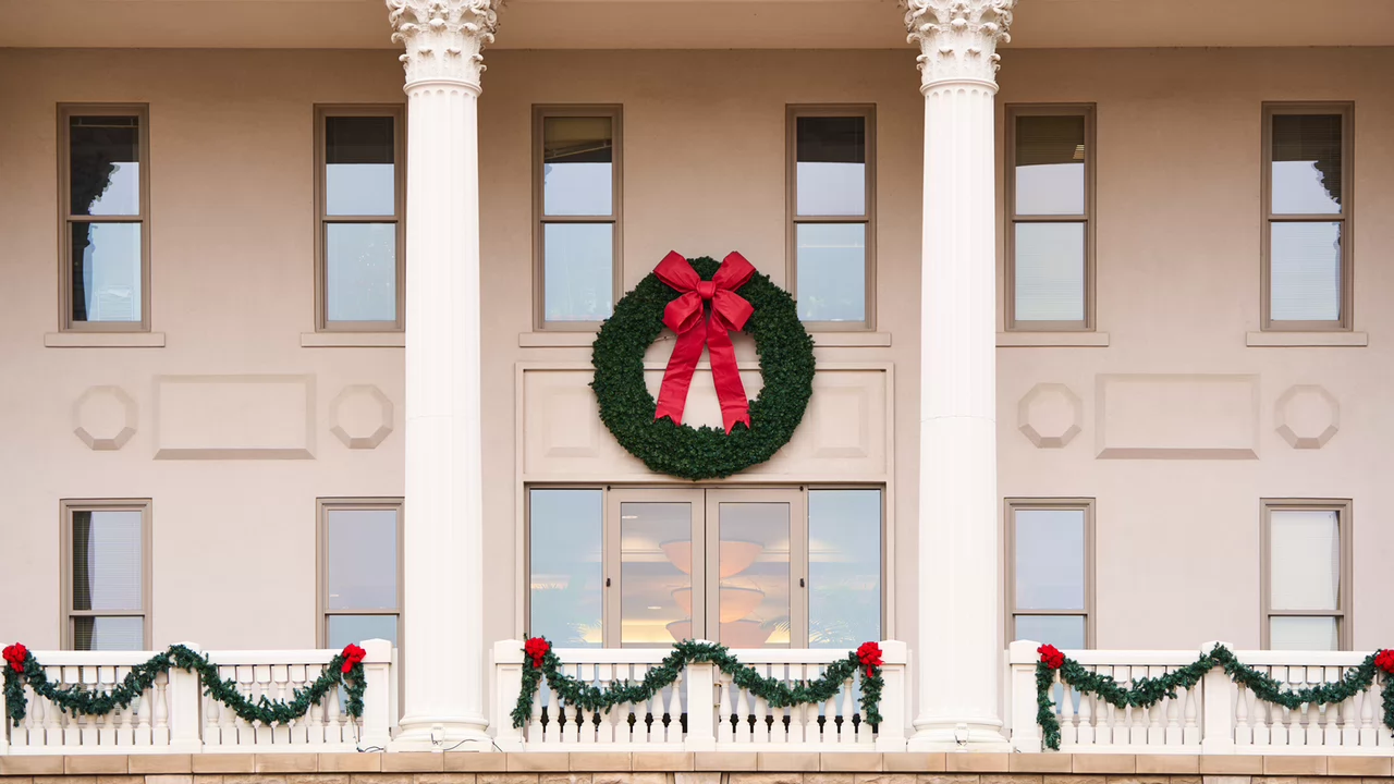Classic building with white columns, adorned for Christmas with a large green wreath and red bow. Festive garland decorates the balcony railing.