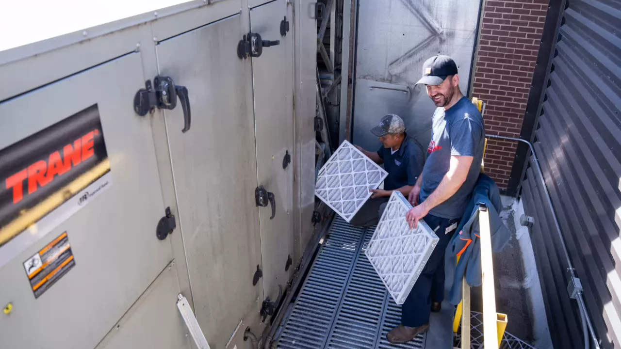 Two technicians replacing air filters in a large Trane commercial HVAC unit during maintenance.