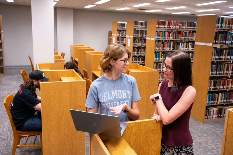 A Bunch library professional talking with a student using a laptop among study cubicles in the Belmont University library.