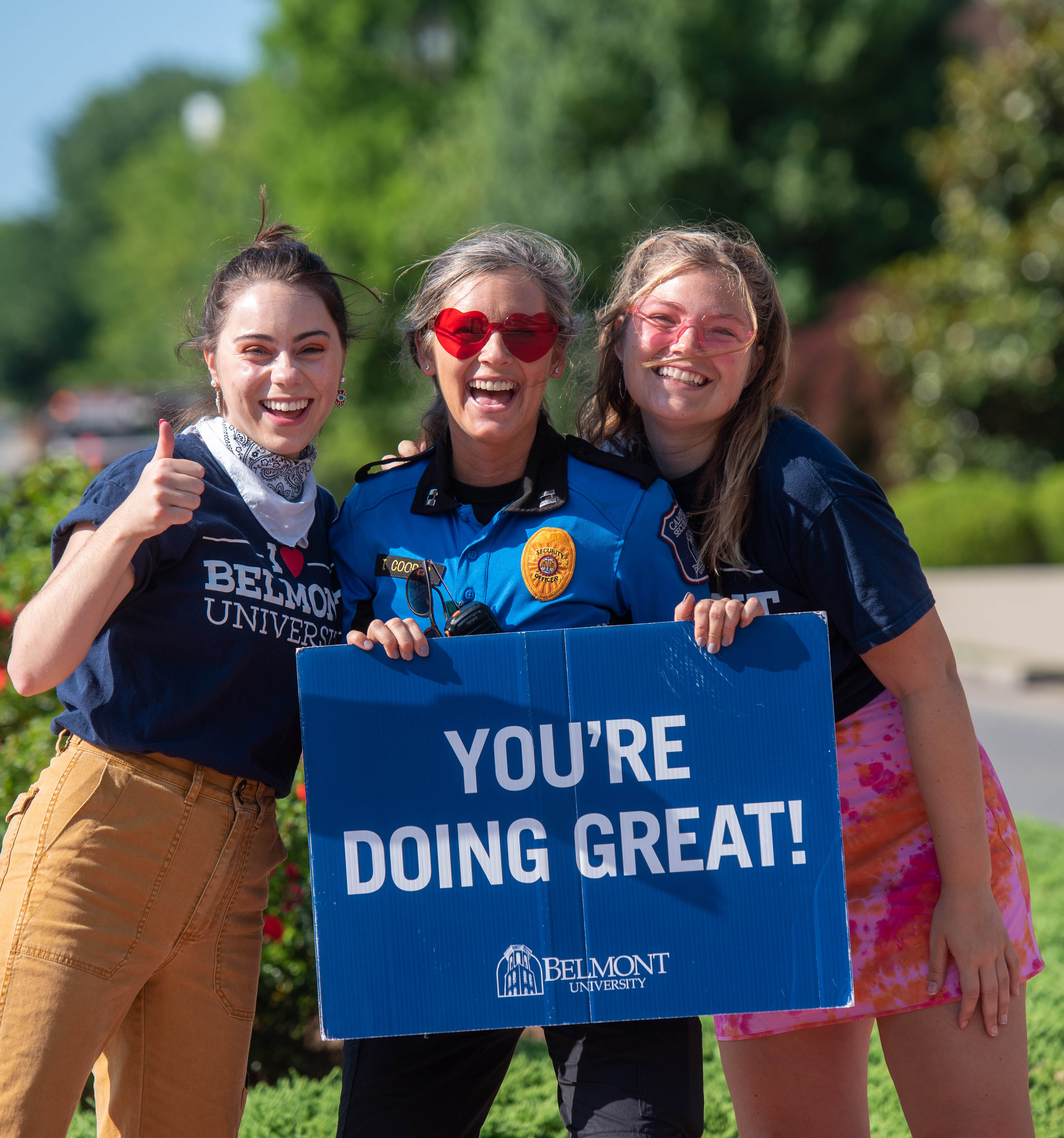 A campus security officer poses with two orientation leaders with a sign that says You're doing great!