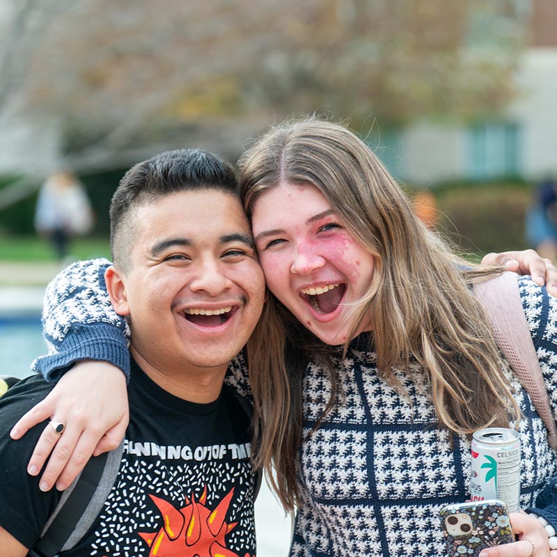 2 students hugging while smiling at the camera