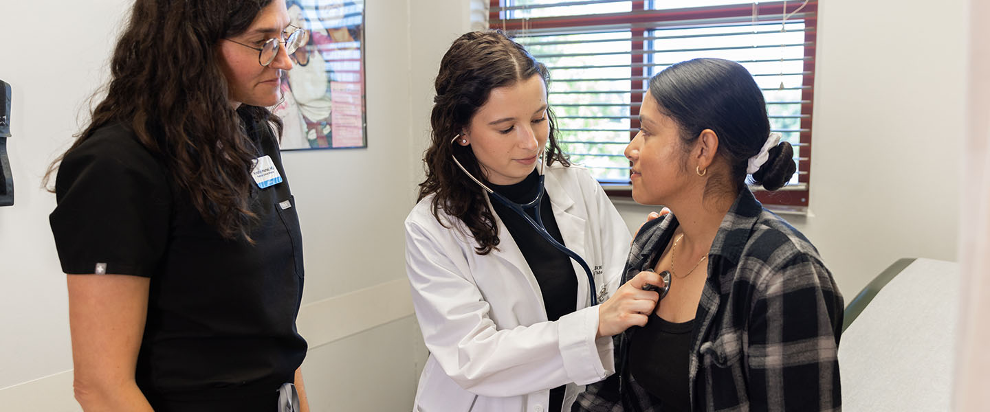 A medical student and clinician examine a patient in an exam room