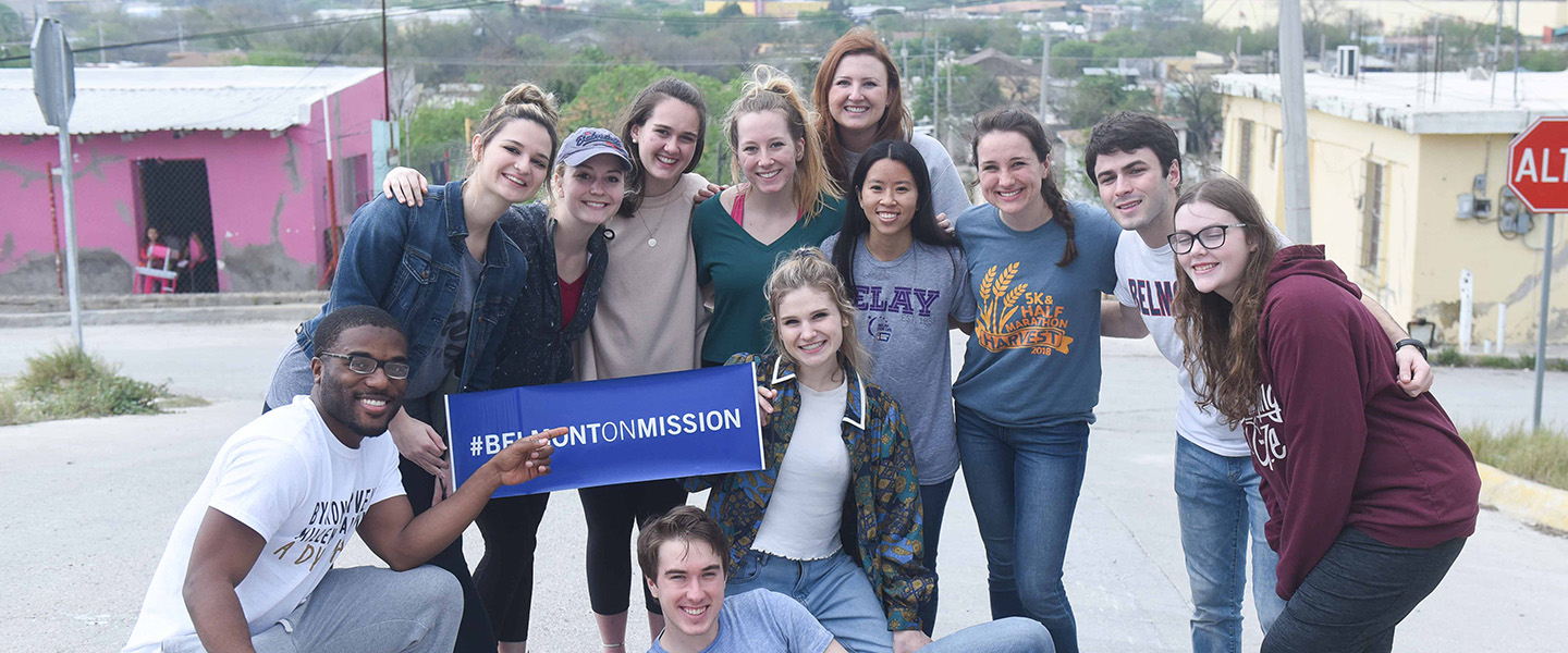 A group of students pose with a "Belmont on Mission" poster.