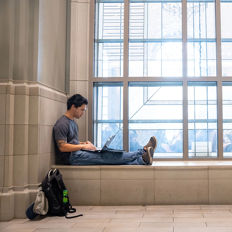 A student studies with a laptop on a window ledge in a Belmont building