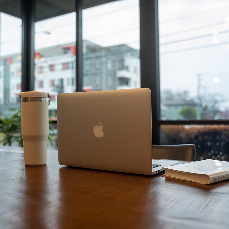 A computer, water bottle, and book sitting on a table in a coffee shop