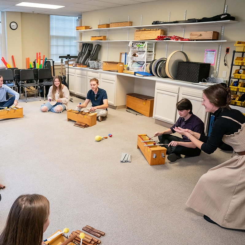 Belmont students seated on the floor with instruments being led by an instructor.