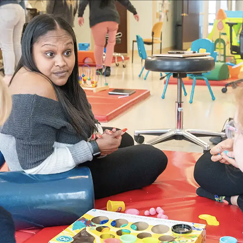 An indoor photo of two Occupational Therapists seated and engaging with pediatric patient