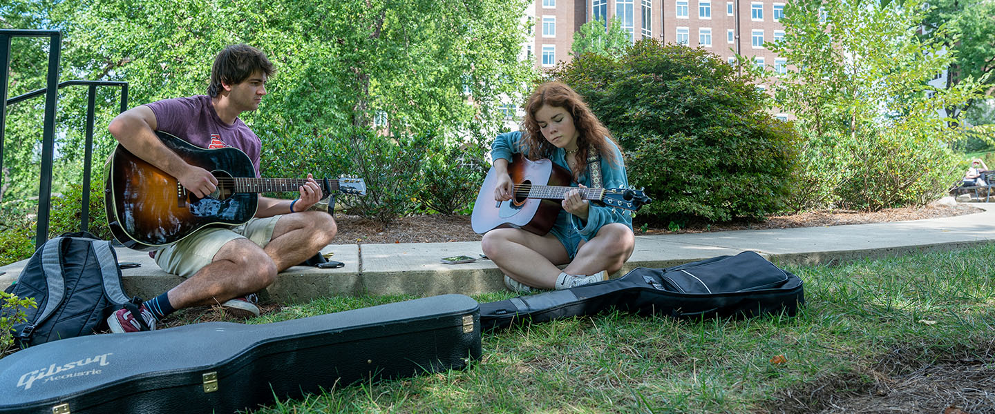 Two students playing music under a tree