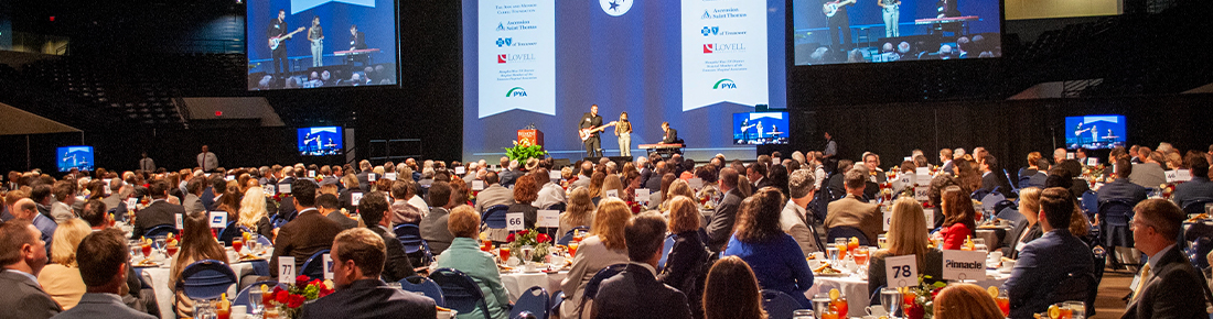 Musicians performing on a stage in front of a large audience seated at tables