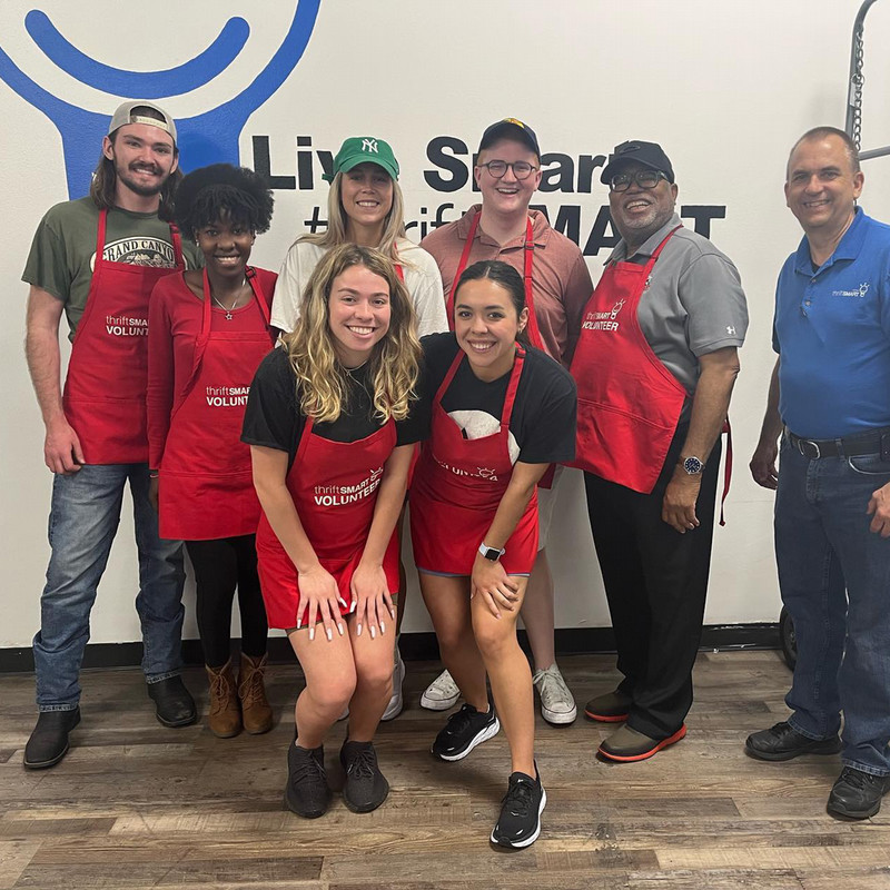 a group of students and a professor smile while wearing red Thriftsmart aprons