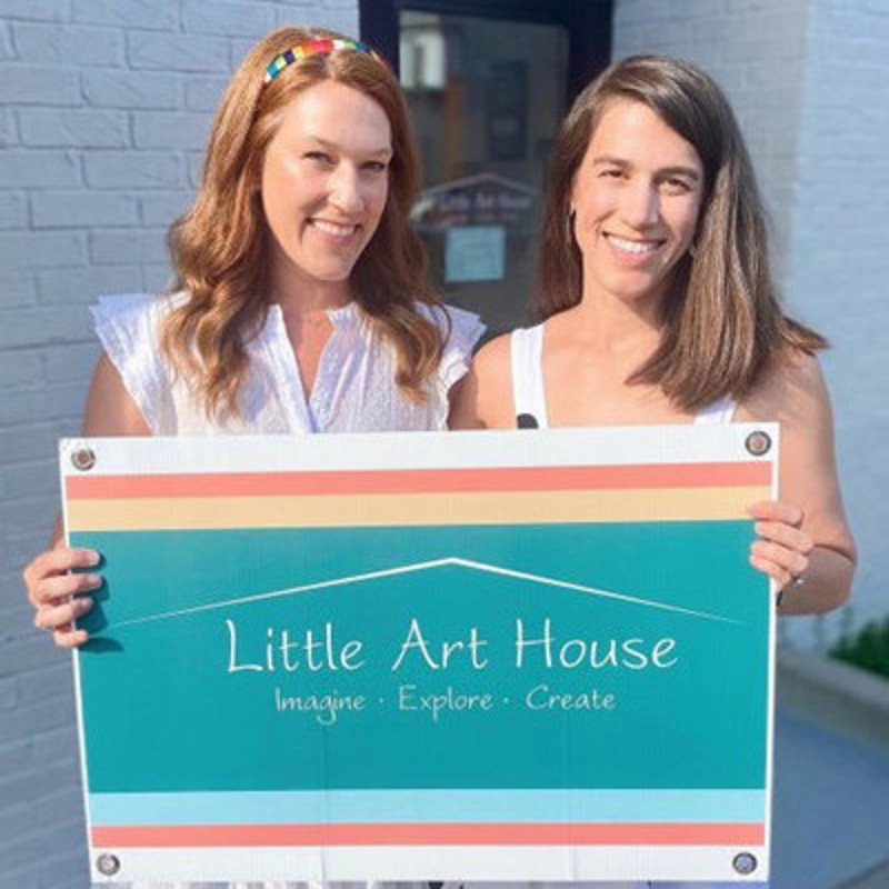 Emma and Leighton smile while holding a sign for Little Art House